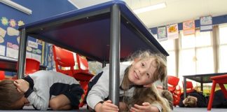 Enner Glynn student Ava Frater, 5, takes cover under a desk as her class practices for the nation-wide Civil Defence Shakeout on September 26. Photo: Andrew Board.