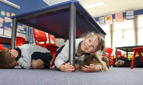 shakeout15 Enner Glynn student Ava Frater, 5, takes cover under a desk as her class practices for the nation-wide Civil Defence Shakeout on September 26. Photo: Andrew Board.