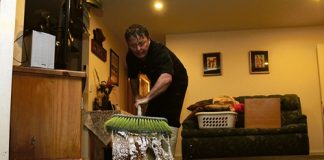 Stoke resident Brendan Sinnot sweeping water out of his neighbour’s home after it was flooded on Sunday night. Photo: Andrew Board