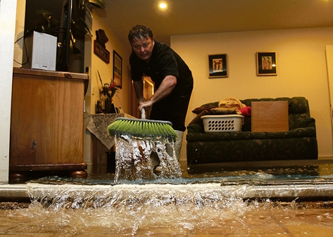floodstoke 054 Stoke resident Brendan Sinnot sweeping water out of his neighbour’s home after it was flooded on Sunday night. Photo: Andrew Board